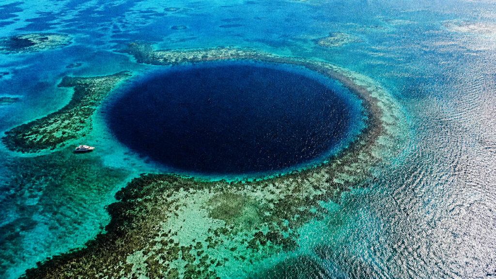 lubang raksasa blue hole di laut dengan air biru gelap kontras di tengah laut jernih
