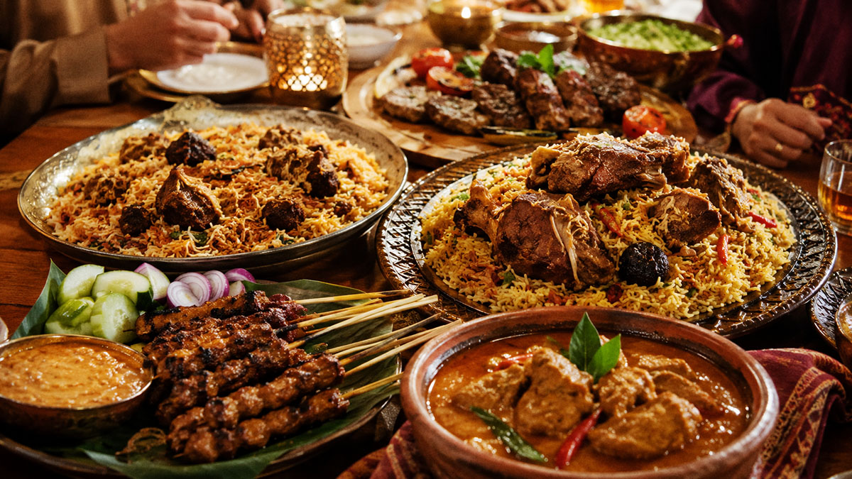 Aneka makanan khas Idul Adha dari berbagai negara seperti sate Indonesia, biryani India, dan kabsa Arab Saudi di meja makan hangat