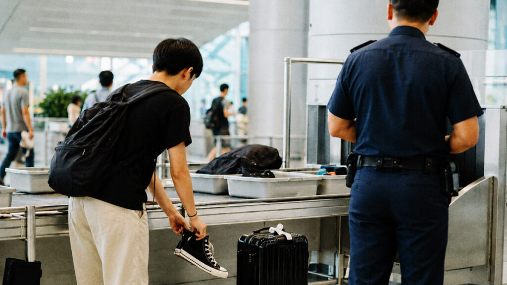 Penumpang melepas sepatu sneakers saat pemeriksaan keamanan di bandara.