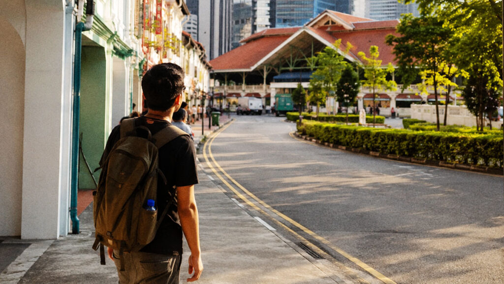 Wisatawan berjalan di kawasan kota Singapura yang bersih dan tertata saat mencari tempat makan warung tenda di tengah deretan bangunan modern dan shophouse bersejarah.